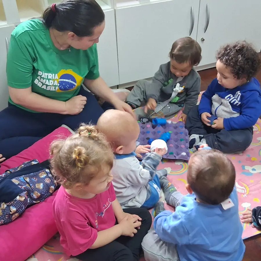 Professora sentada no tapete com bebês e crianças pequenas brincando