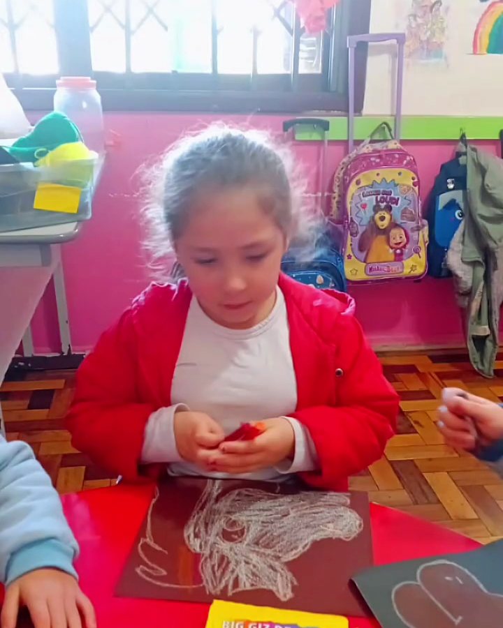 Menina desenhando com giz numa prancha preta na mesa vermelha