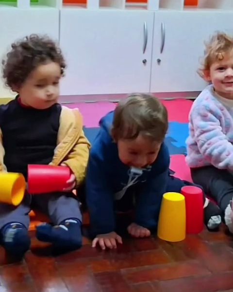 Crianças sentadas no tapete na aula de musicalização com copos coloridos