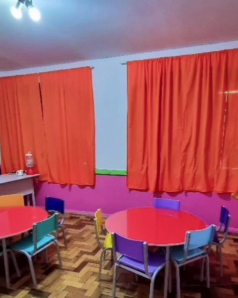 Sala do Pré com mesas vermelhas e cortinas laranja
