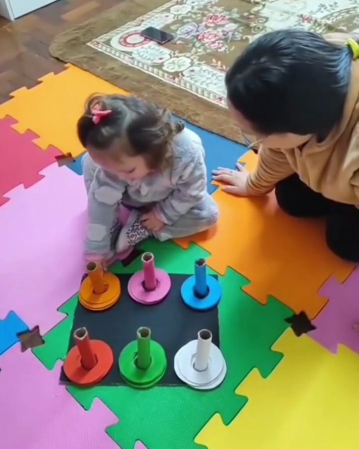 Menina brincando de encaixe no tapete colorido com a professora